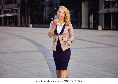 Female Manager In Business Suit Talks By Phone Using Speakerphone.