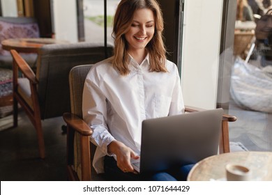 Female manager having a video call via laptop in coffee shop, hipster freelancer in casual style sitting relaxed at cafe near the window and having a Skype call, smiling girl laughing watching video