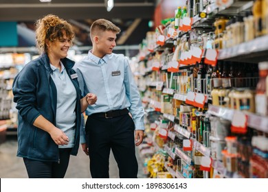 Female Manager Helping New Male Trainee At Grocery Store. Man On Holiday Job Getting Help From Manager At Supermarket.