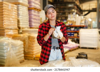 Female Manager Keeps Records Of Bulk Construction Materials In The Warehouse, Writing Down The Data On Smartphone