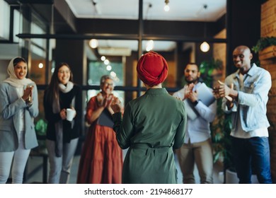 Female manager receiving an applause from her business colleagues during a staff meeting. Rearview of a successful businesswoman giving a speech in a multicultural workplace. - Powered by Shutterstock