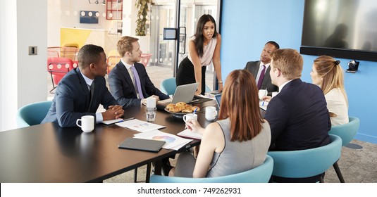 Female manager stands addressing colleagues in meeting room