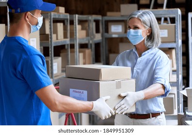 Female manager supervisor wearing face mask preparing fast drop shipping safe delivery giving parcels packages boxes to male courier taking ecommerce orders to deliver standing in warehouse storage. - Powered by Shutterstock