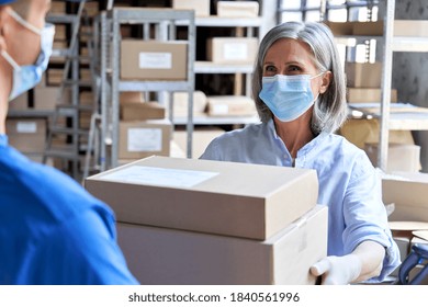 Female Manager Worker Wearing Face Mask Holding Fast Drop Shipping Safe Delivery Packages Giving Parcels Shipment Boxes To Male Courier Taking Ecommerce Orders To Deliver In Warehouse Storage.