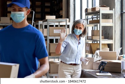 Female Manager Worker Wearing Face Mask Waving Hand To Courier Holding Fast Drop Shipping Safe Delivery Packages Parcels Shipment Boxes Delivering Ecommerce Dropshipping Orders From Warehouse Storage.