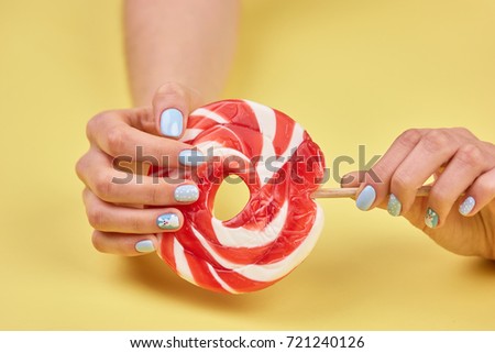 Female manicured hands with lollipop. Woman hands with beautiful manicure holding large colorful lollipop on yellow background.