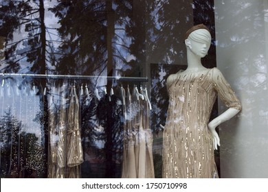 Female mannequin in a beautiful beige, golden elegant evening cocktail dress with sequins. Shop window with fashionable dresses.