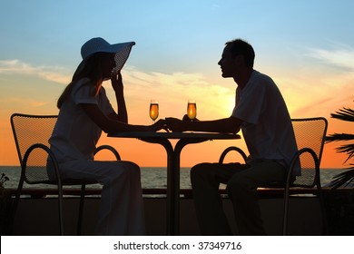 Female and man's silhouettes on sunset sit at table with two glasses outdoor