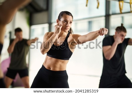 Female martial artist practicing punches while having exercise class at health club.