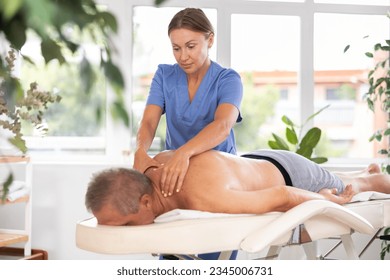 Female massage therapist working out back zone of male patient during deep tissue back massage