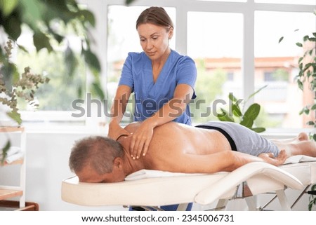 Female massage therapist working out back zone of male patient during deep tissue back massage