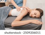 Female masseur massaging back and shoulder blades of young woman lying on massage table. Concept of massage spa treatments.
