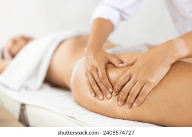 Female masseuse doing thigh massage closeup to young woman client - Powered by Shutterstock