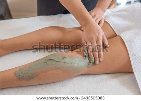 Female masseuse performs mud treatment with leg massage for a woman in a spa and beauty center 