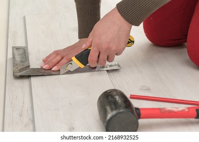 Female master cuts quartz vinyl floor with a stationery knife, floor installation, woman performs repair work.