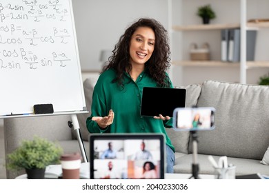 Female Math Teacher Making Video Conference Chat With Diverse Group Of Students Using Laptop And Cellphone On Tripod, Holding Showing Tablet With Empty Screen With Copy Space For Mockup, Explaining