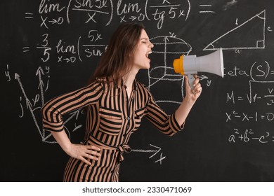 Female Math teacher shouting into megaphone near blackboard in classroom - Powered by Shutterstock