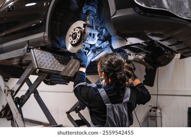 Female mechanic inspecting the undercarriage of a car lifted on a hydraulic ramp in a professional auto repair shop - Powered by Shutterstock