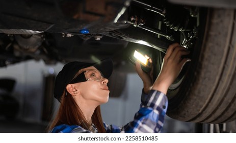 A female mechanic inspects a lifted car. A girl at a man's work. - Shutterstock ID 2258510485