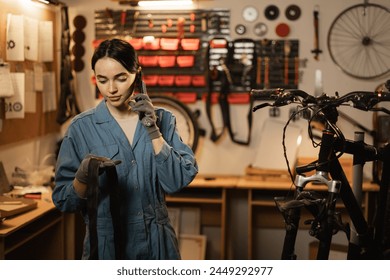 Female mechanic takes order by mobile phone standing in bicycle workshop near bike. Mechanic talking on mobile phone after fixing bike. Copy space - Powered by Shutterstock