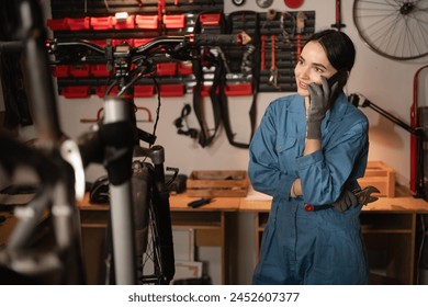 Female mechanic talking on mobile phone. Girl calls after fixing bike in atmospheric garage. Copy space - Powered by Shutterstock