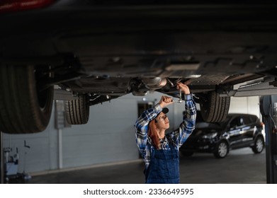 Female mechanic unscrew the nuts on the bottom of the car that is on the lift. A girl at a man's work. - Powered by Shutterstock