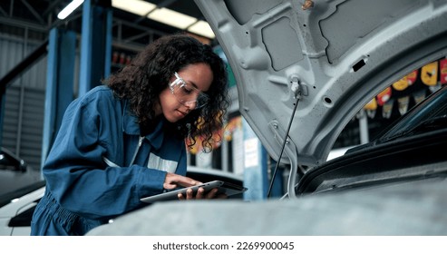 Female mechanic uses tablet computer with diagnostics software checking car engine. Specialist inspecting the car in order to find broken components inside the engine bay. Car Service - Powered by Shutterstock