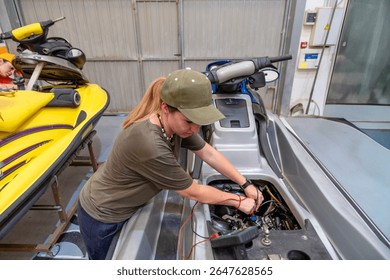 Female mechanic using multimeter checking engine of personal watercraft during maintenance in a jetski repair shop