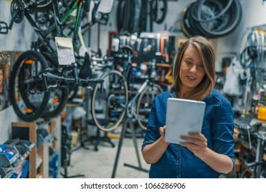 Female mechanic at work. Using a tablet while fixing a bicycle. Female bicycle repair technician using digital tablet in bicycle shop. Mechanic woman checking something on a tablet-pc and checklist. - Powered by Shutterstock