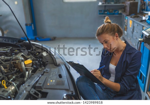 Female mechanic\
working in auto repair shop. Beautiful woman working at car service\
station, filling papers on clipboard. Attractive female mechanic\
enjoying working at her garage.\

