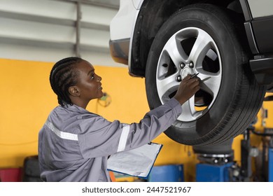 Female mechanic working at garage. Female mechanics checking tire wheel underneath lifted car at auto car repair service. Car service and Maintenance concept - Powered by Shutterstock