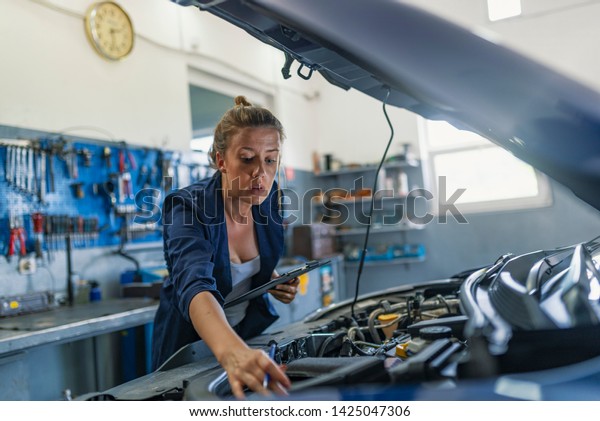 Female\
mechanic working on car. A Mechanic woman working on car in her\
shop. Technician woman working in auto repair workshop. Mechanic\
repairs the engine of a car in her\
workshop.