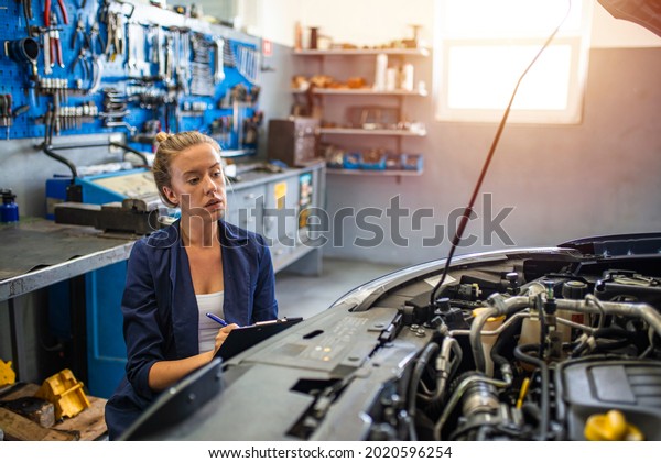 Female mechanic working on car tyre service.\
Portrait Of Female Auto Mechanic Working Underneath Car. Portrait\
of smiling young female mechanic inspecting a CV joing on a car in\
auto repair shop