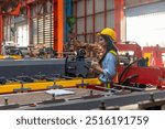 Female mechanical engineer in safety suit checking or inspecting a machine in metal sheet production system. Using technology for iron sheet formation and shape. Young factory worker examining machine