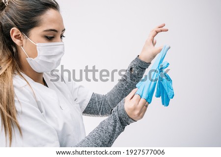 Female medic in protective mask taking off used latex gloves after work in clinic during coronavirus pandemic