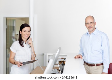 Female Medical Assistant Answers Phone Call At Reception While Patient Is Waiting