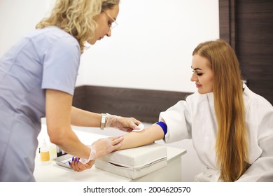 Female medical practitioner smearing arm of woman with alcohol pad before taking blood sample in hospital - Shutterstock ID 2004620570