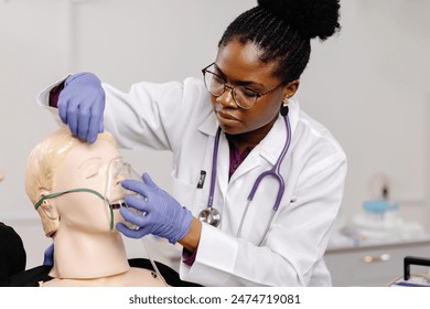 A female medical professional wearing a white coat and stethoscope practices applying an oxygen mask to a mannequin. - Powered by Shutterstock