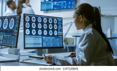 Female Medical Research Scientist Working with Brain Scans on Her Personal Computer, Writing Down Data in a Clipboard. Modern Laboratory Working on Neurophysiology, Science,  Neuropharmacology.