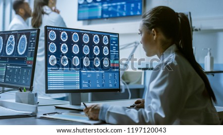 Female Medical Research Scientist Working with Brain Scans on Her Personal Computer, Writing Down Data in a Clipboard. Modern Laboratory Working on Neurophysiology, Science,  Neuropharmacology.