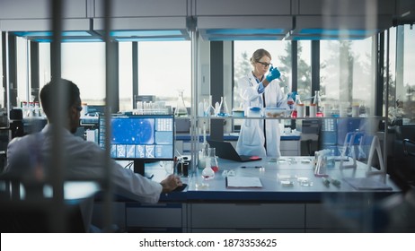 Female Medical Scientist Wearing White Coat And Safety Glasses Uses Micropipette While Examining Testing Sample. Innovative, Experimental Drugs Research, Biotech Development In High-Tech Laboratory