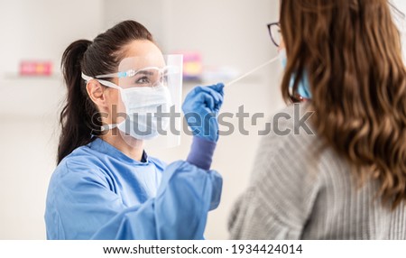 Female medical staff worker wearing protective equipment takes sample from nose of a patient to antigen test for coronavirus.