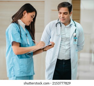 Female Medical Student Is On The Job Clinical Learning With Professional Male Doctor At Medical School Hospital. Woman Intern Doctor Holds Clipboard On The Job Training With Doctor Teacher Lecturer.