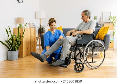 Female medical worker helping senior man in wheelchair doing stretching leg exercises at home. Elderly health care assistance concept. - Powered by Shutterstock