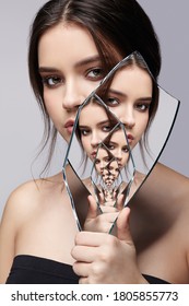 Female With Mirror Shard In Hand Posing On Gray Background. Multiple Reflections In Mirror Splinter.