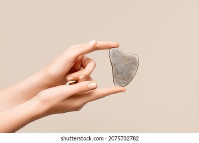 Female Model Hands With Brown Jade Gua Sha Scraper On Beige Background. Spa Body Care Tool. Beauty Care Gua Sha Stone Scraper. Copy Space