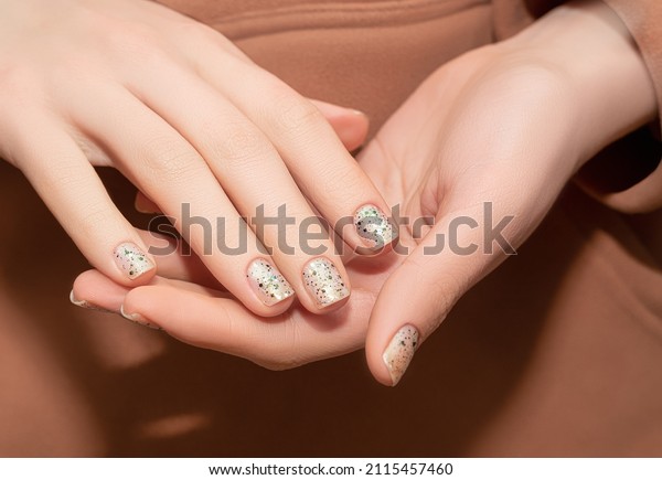 Female model hands with clear nail design.\
Glitter clear nail polish manicure with green nail art. Female\
model with perfect manicure in brown\
hoodie