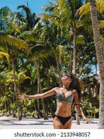 Female model posing in a bikini on a paradise beach with palm trees
				