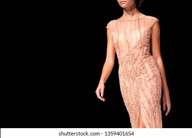 Female Model Walks The Runway In Pink Dress Isolated On A Black Background During A Fashion Show. Fashion Catwalk Event Showing New Collection Of Clothes. Single Female Model In Beautiful Dress.