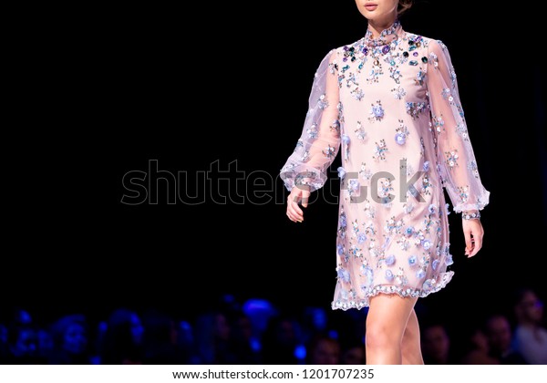 Female model walks the runway in pink dress\
isolated on a black background during a Fashion Show. Fashion\
catwalk event showing new collection of clothes. Single female\
model in beautiful\
dress.